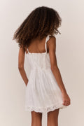 Tween girl wearing a white lace sleeveless dress against a plain background