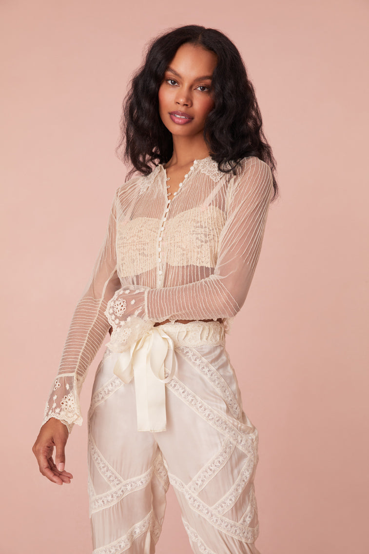 Long sleeve sheer cream blouse with scallop lace at the collar and the ruffled cuff sleeves. Delicate pintucks throughout with self-covered buttons down center front and floral embroideries.