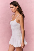 Woman wearing a white lace sleeveless mini dress against a pink background