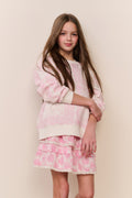 Young girl wearing a pink and white outfit against a beige wall.