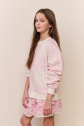 Young girl wearing a pink and white outfit against a beige wall.