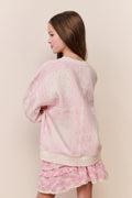Young girl wearing a pink and white outfit against a beige wall.