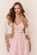 Woman wearing a cream and brown Cardigan with floral and western star patterns and pink dress on a beige background