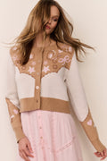 Woman wearing a cream and brown Cardigan with floral and western star patterns and pink dress on a beige background