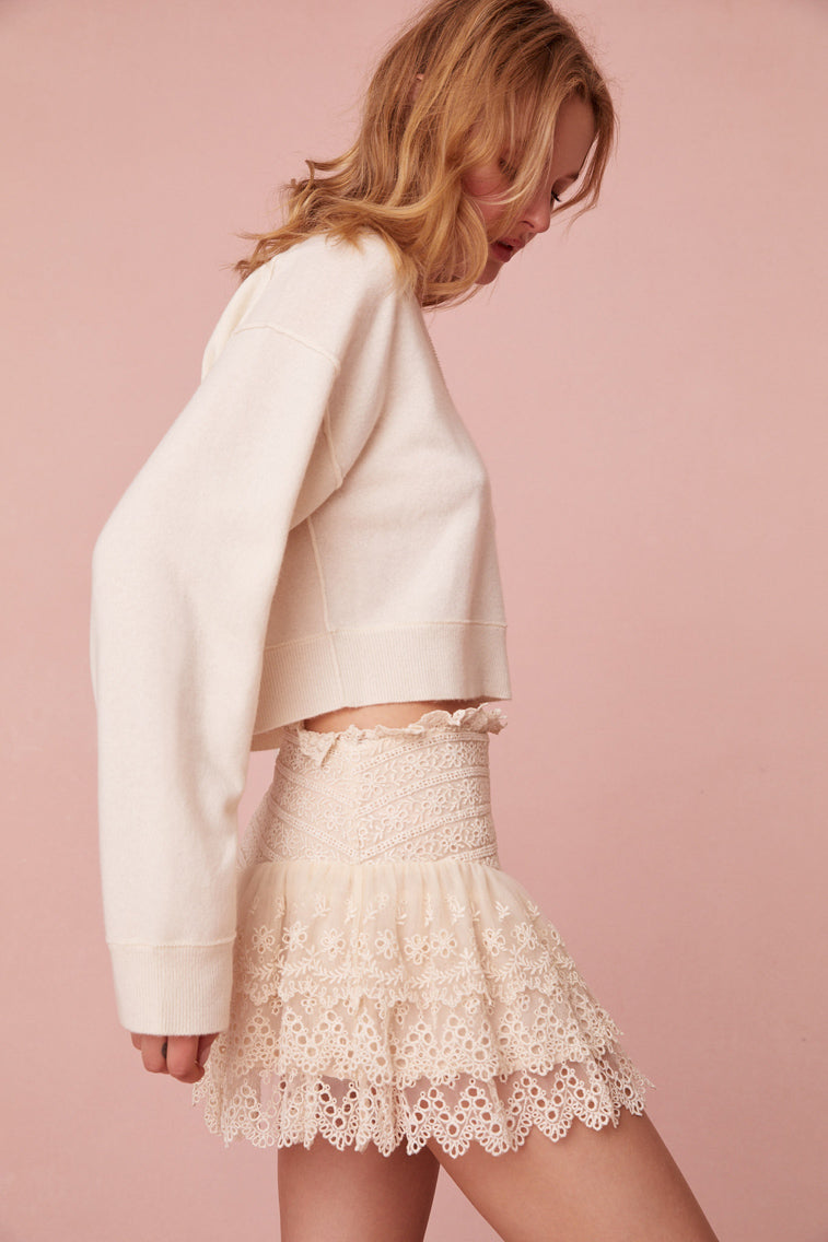 Cream mini skirt with embroidered mesh fabric. The piece has a fixed waist that hikes at the side seam and ruffles that create ethereal, dreamy tiers.