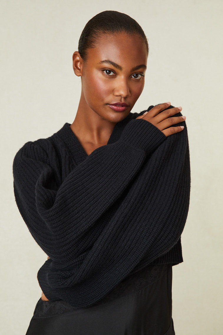 Black cashmere-wool blend cropped sweater, has a v-neck that descends to three buttons at center front. Pleated blouson sleeves extend to ribbed cuffs at opening.