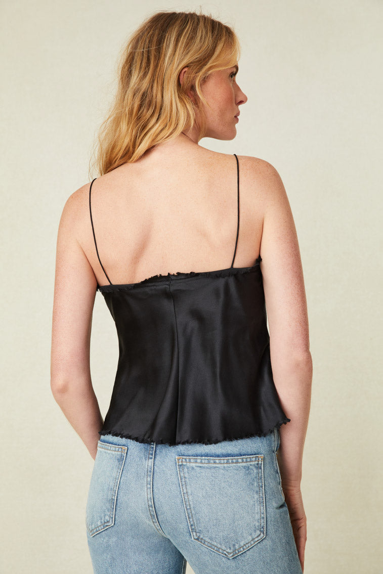 Model wearing black camisole top with ruffle detail on neckline, raw hem, and removable rosette pin.