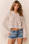 Woman wearing a white eyelet button down and denim shorts with lace trim on a neutral background
