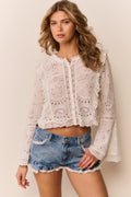 Woman wearing a white eyelet button down and denim shorts with lace trim on a neutral background