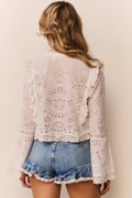 Woman wearing a white lace blouse with denim shorts against a plain background