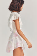 Woman wears white ruffle cropped top with mini white and pink tie-dye ruffle skirt against beige background