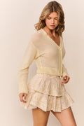Woman wearing a pale yellow-colored cardigan over a patterned ruffle skirt on a plain background