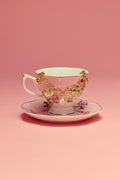 Teacup and saucer with a gold bracelet on a pink background