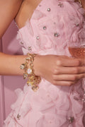 Close-up of a person wearing a pink floral dress with embellishments and a gold bracelet.