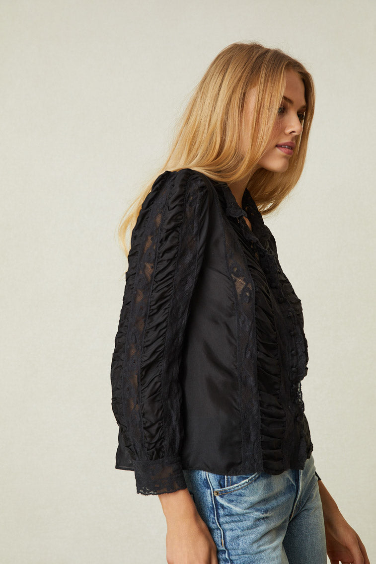 Side image of model wearing black long sleeve blouse with button up front, lace detail, and puff shoulders.