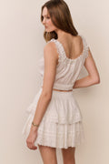 Woman wearing a white lace top and skirt set against a plain background
