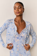 Woman wearing a light blue floral cardigan over a matching dress against a plain background