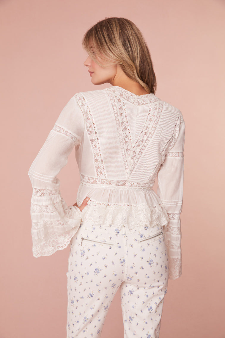 Long sleeved blouse with a shaped waist that releases into a peplum with laces throughout. The front has center front buttons with tiny tie details.