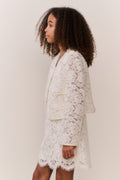 Tween wearing a white lace jacket and mini dress outfit on a plain background