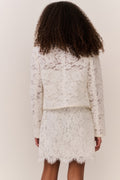 Tween wearing a white lace jacket and mini dress outfit on a plain background