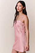 Woman wearing a pink satin slip dress with bow design against a plain background