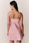 Woman wearing a pink satin slip dress with bow design against a plain background
