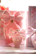 Pink mini eau de parfum bottle with bow and gold cap, gift set box in background
