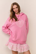 Woman wearing a pink hoodie with a heart design and a matching skirt on a beige background