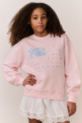 Girl wearing a pink american flag sweatshirt and white lace skirt on a plain background