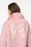Pink coat with a white bow design on the back, worn by a person.