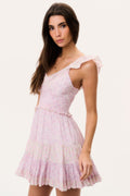 Woman wearing a pink mini dress with ruffled cap sleeves and open back on a white background