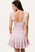 Woman wearing a pink mini dress with ruffled cap sleeves and open back on a white background