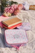 Floral-patterned lunch bag on a picnic blanket with books and flowers