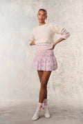 Person wearing a light pink sweater and skirt with a white background