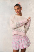 Woman wearing a pink and white patterned sweater and skirt against a light background