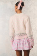 Person wearing a light pink sweater and floral skirt with a textured white background