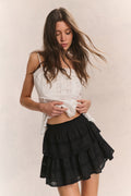 Woman wears white ruffle cropped top with mini black ruffle skirt against beige background