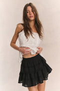 Woman wears white ruffle cropped top with mini black ruffle skirt against beige background