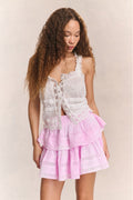 Woman wears white ruffle lace top with mini pink ruffle skirt against beige background