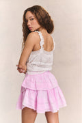 Woman wears white ruffle lace top with mini pink ruffle skirt against beige background