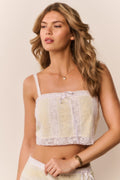 Woman wearing a white and yellow lace cropped top with matching skirt against a beige background