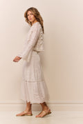 Woman wearing a white lace eyelet maxi skirt and matching long sleeve blouse against a plain background