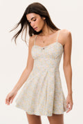 Woman wearing a floral mini dress with thin straps on a plain background