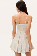 Woman wearing a floral mini dress with thin straps on a plain background