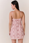 Woman wearing a pink lace mini dress with bow pattern embellishments on a white background