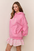 Woman wearing a pink hoodie and patterned skirt against a beige background