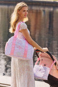 Woman pushing a stroller with a matching bag by a body of water