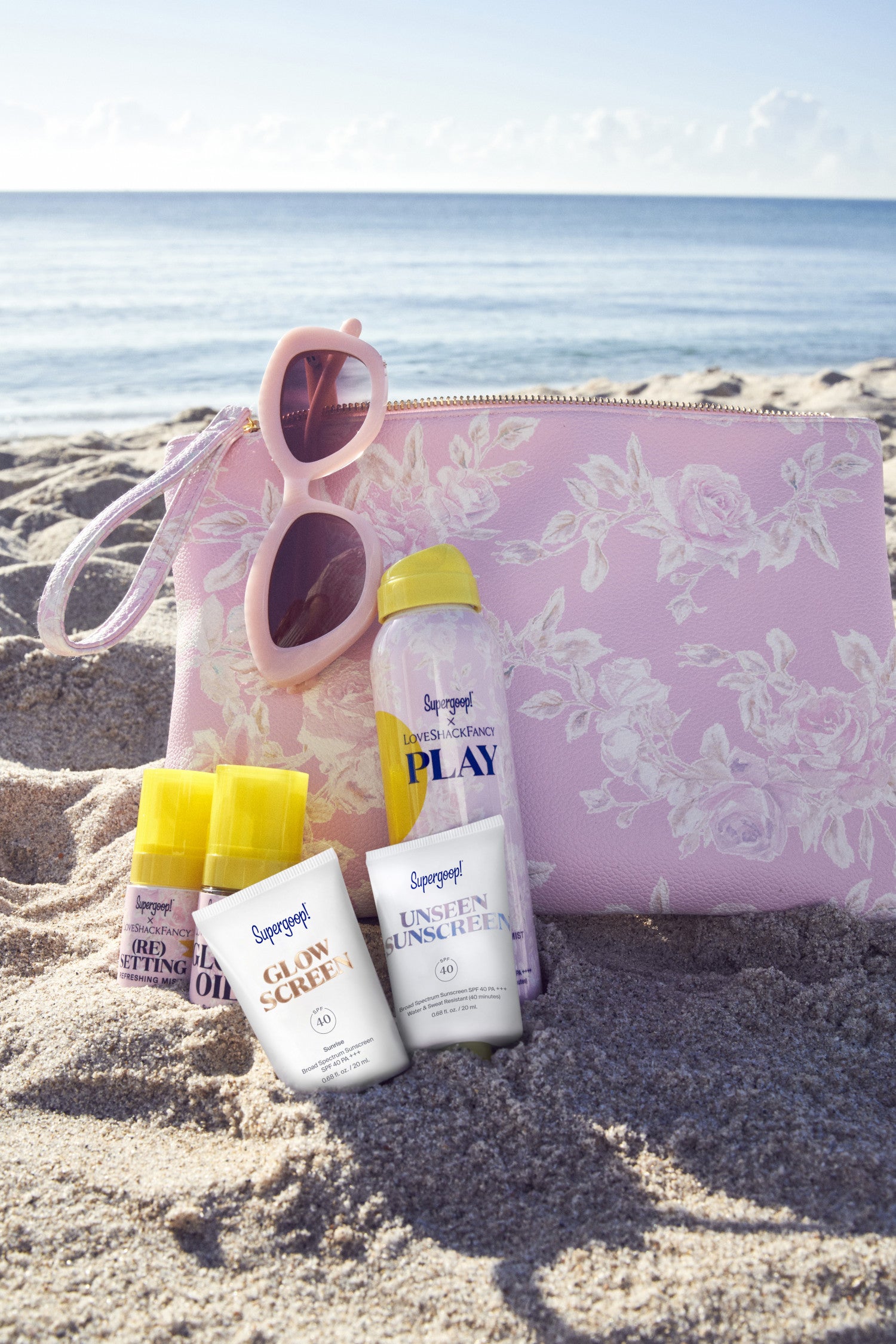 Supergoop products in LSF floral print with LSF pouch and sunglasses sitting on beach