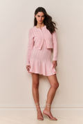 Woman wearing a pink knitted dress and cardigan set against a plain background