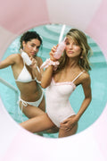 Two women in swimsuits with a pink bottle in a circular frame.
